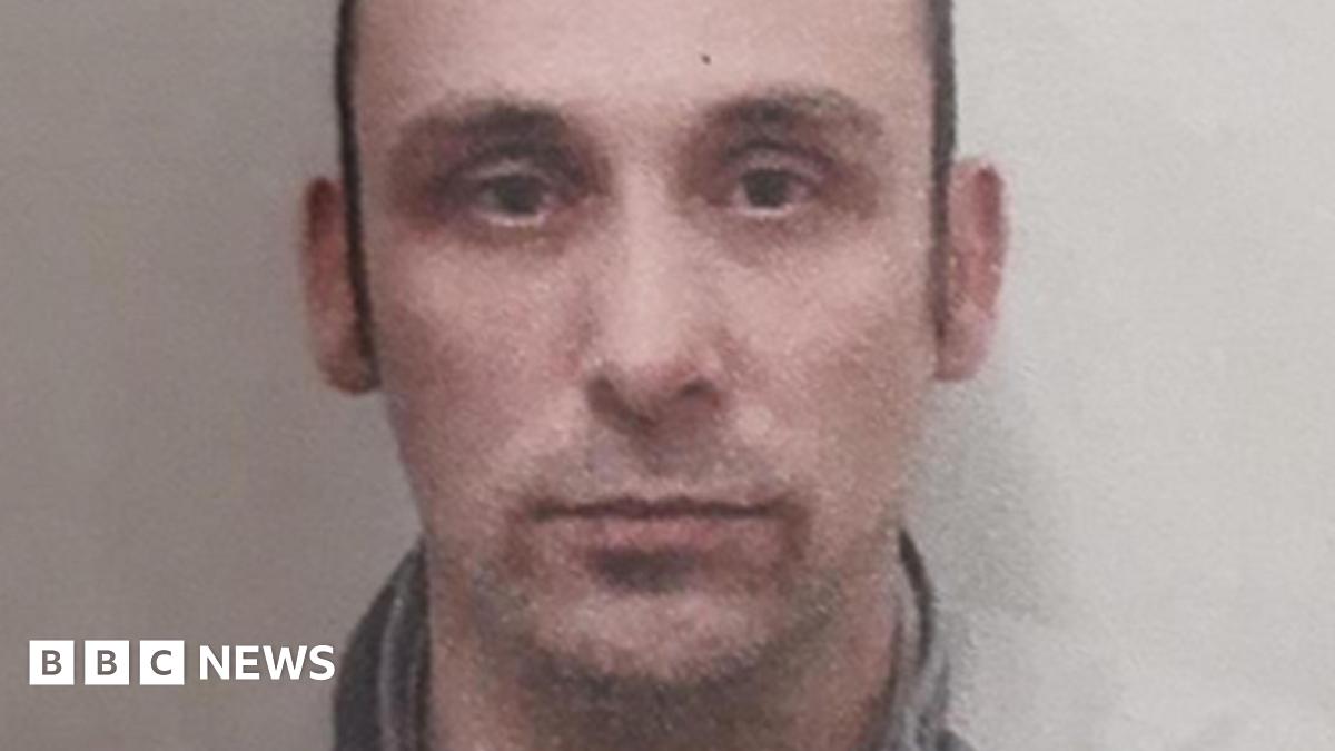 Daniel Washbourne is looking at the camera with a stubbly moustache. He has short brown hair. The image is low-quality.