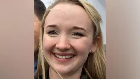 Andrea Brady A close-up photo of Jessica Brady who is smiling broadly and looking directly at the camera, with long blonde hair, brown eyes and an earring visible in her left ear