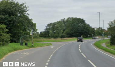 A Google Street image of a bus stop to the left of a road.