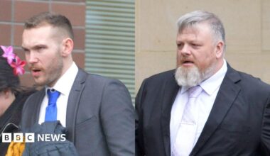Two men in grey suits walk into court, both wearing smart shirts and ties. Both have short hair with groomed facial hair.