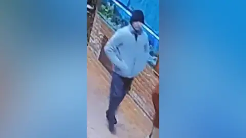 Police handout Daniel Washbourne is walking down a street, wearing a cream fleece, blue tracksuit bottoms, blue hat and black trainers.