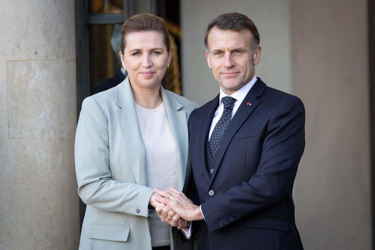 Mette Frederiksen and Emmanuel Macron clasping hands.