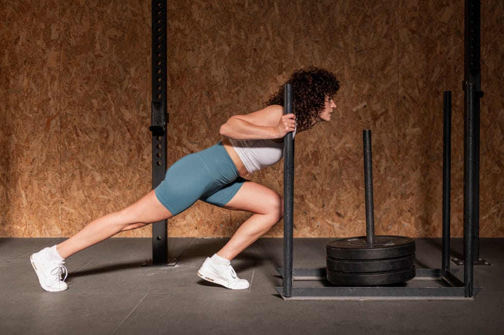 Athletic woman doing sled training at gym person performing a sled push exercise in a gym