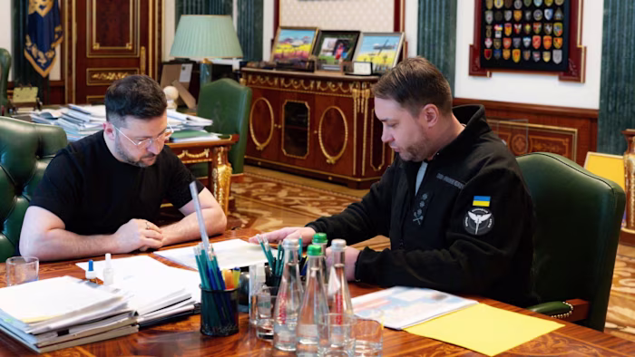 Volodymyr Zelensky and Kyrylo Budanov sit at a desk in an official office, reviewing documents together.
