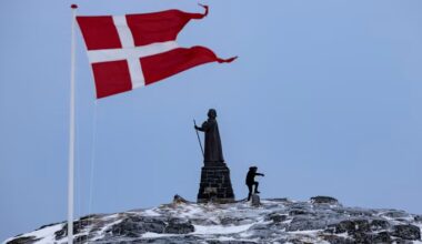 A Danish flag flutters near the Hans Egede statue as a person walks on a snow-dusted hill in Nuuk, Greenland.