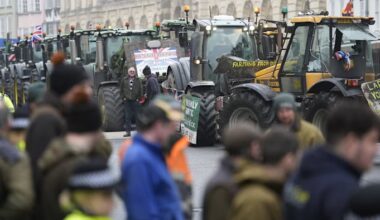 Several tractors with protest signs are lined up in the street as farmers and police gather outside the Oxford Farming Conference.