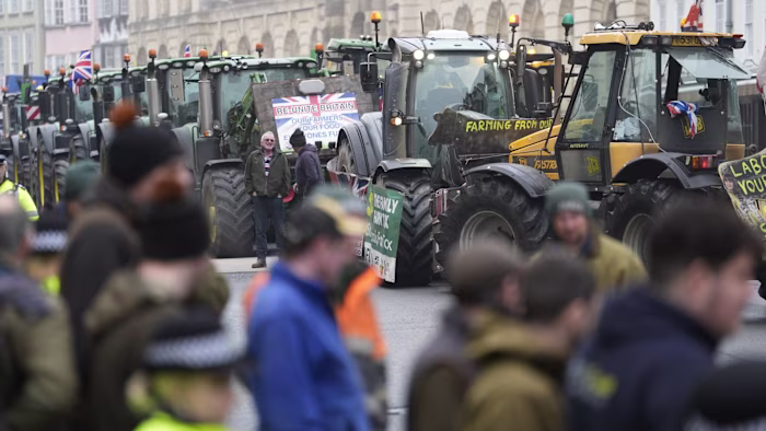Several tractors with protest signs are lined up in the street as farmers and police gather outside the Oxford Farming Conference.