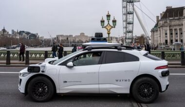 A white Waymo self-driving car with sensors on its roof is stopped on a London street near the London Eye.