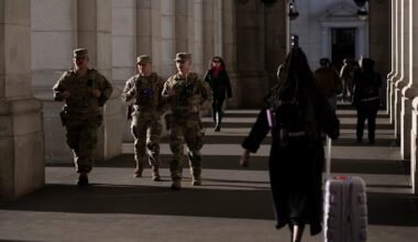 Three National Guard members in uniform walk past travelers in a colonnade at Union Station.