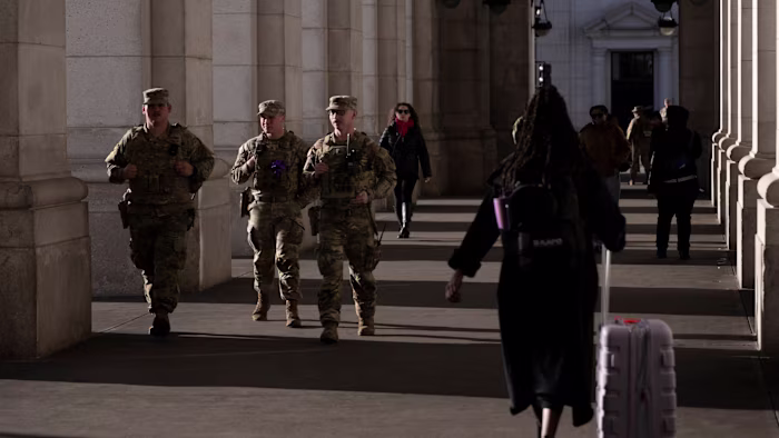 Three National Guard members in uniform walk past travelers in a colonnade at Union Station.