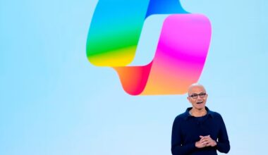 Satya Nadella speaks on stage in front of a large colorful Copilot logo during a Microsoft event.