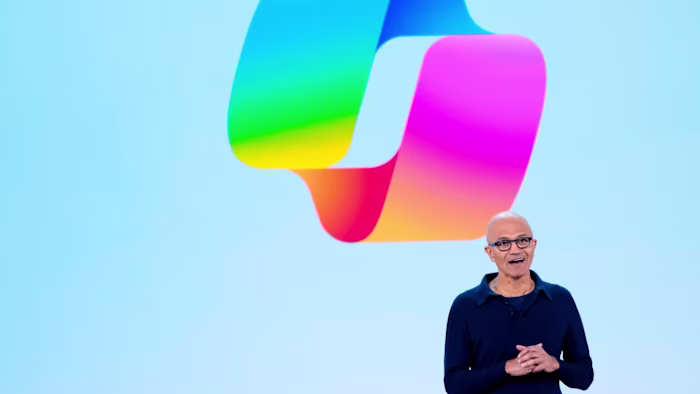 Satya Nadella speaks on stage in front of a large colorful Copilot logo during a Microsoft event.
