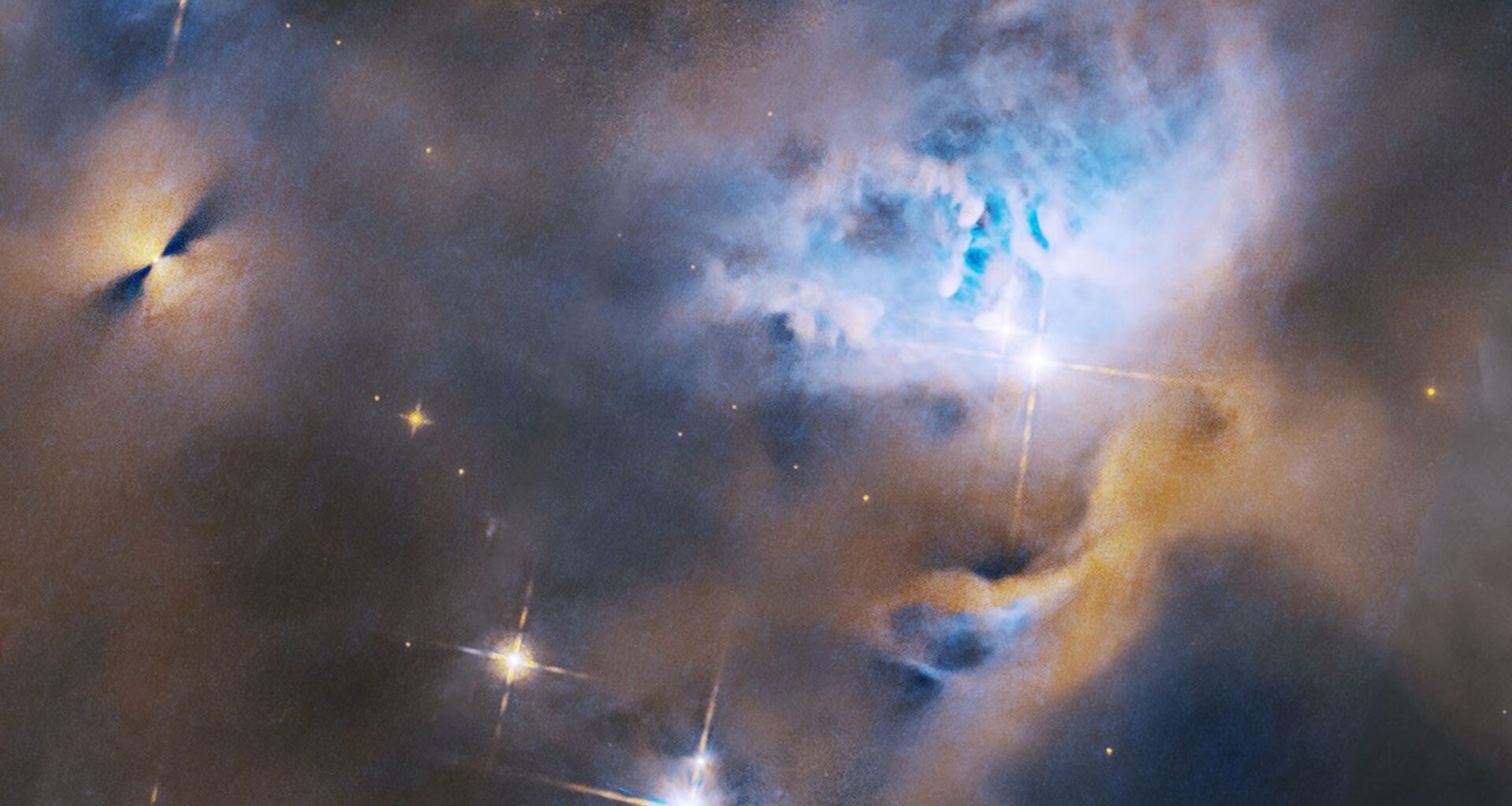 Within a ghostly blue and orange cloud of gas and dust, several stars shine brightly. To the upper left is a protoplanetary disk, appearing as a bright point flanked on either side by fan-shaped shadows. To the center right, stars are nestled in a cavity in the gas and dust.