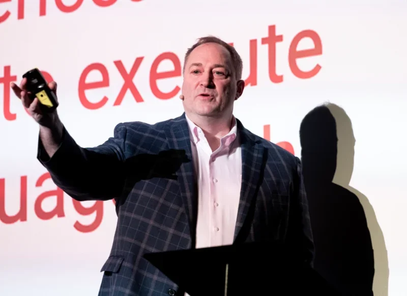 Anthony Katsur, CEO, IAB Tech Lab speaking on stage with close-up words on presentation behind him