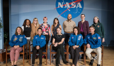 A group of people pose in an auditorium in front of a blue background with a NASA meatball insignia.