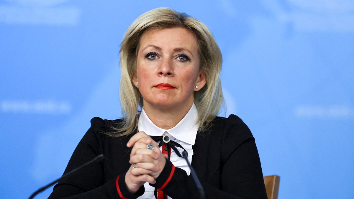 A senior government spokeswoman listens during a formal briefing inside a conference hall.