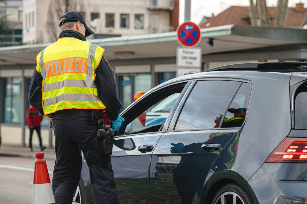 German police officer wearing a high-visibility vest checks a car at a roadside border control point.