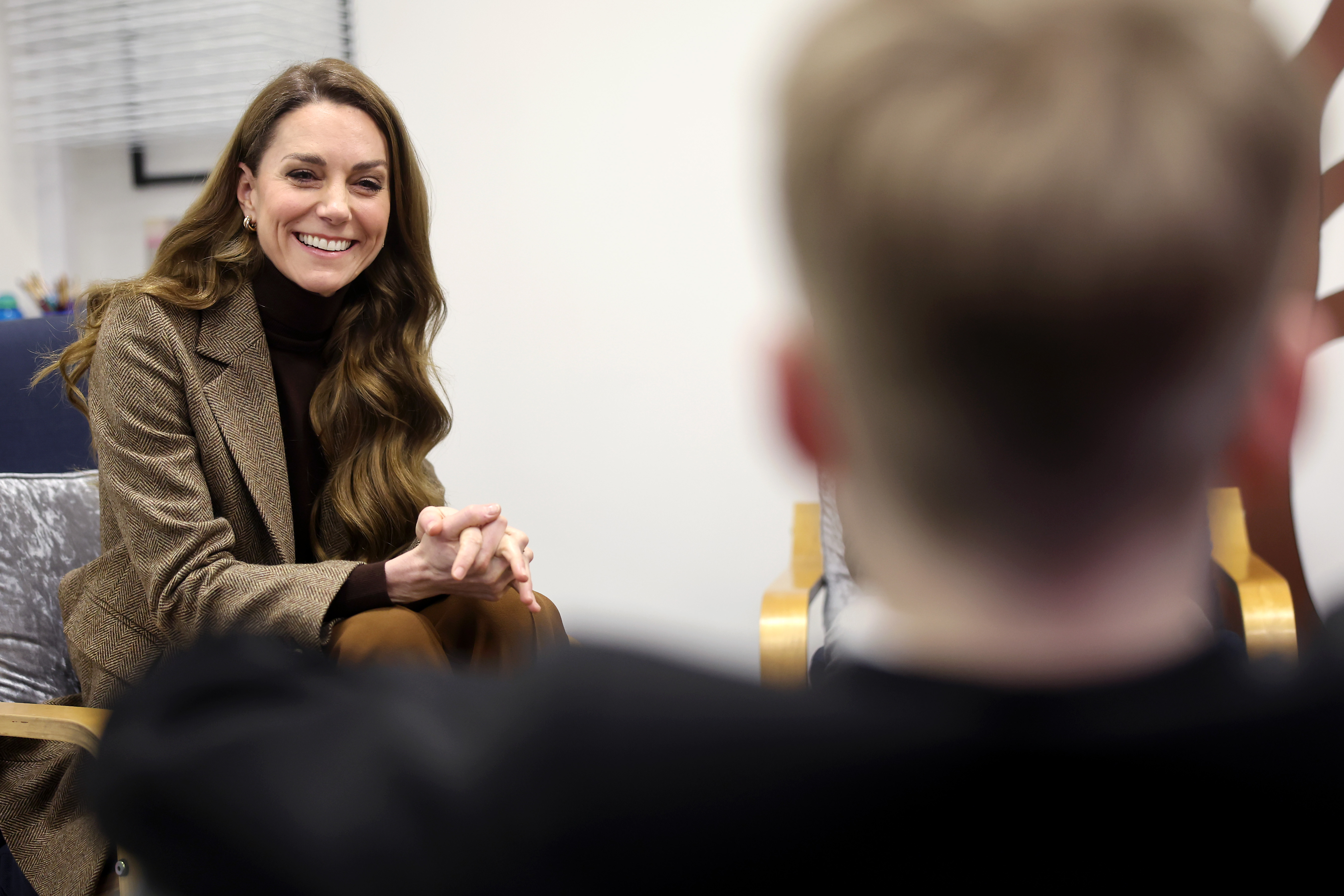 Princess Kate wearing a brown blazer and smiling talking to a boy