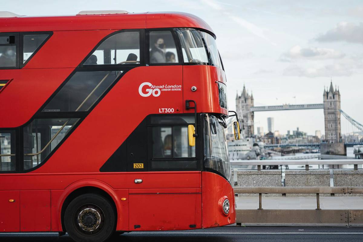 a london bus crossing a bridge with a view of tower bridge in the background