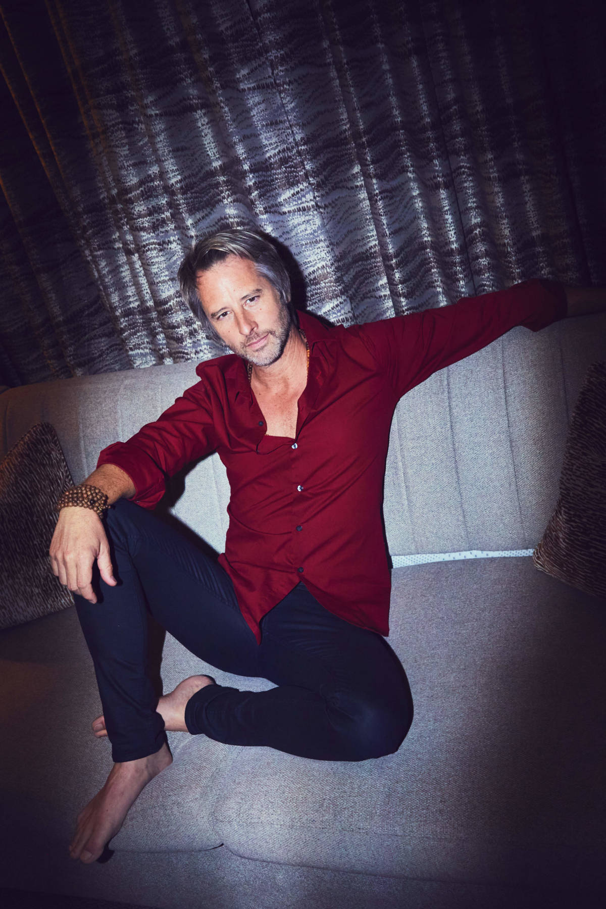 press photo of chesney hawkes on sofa wearing red shirt and black jeans