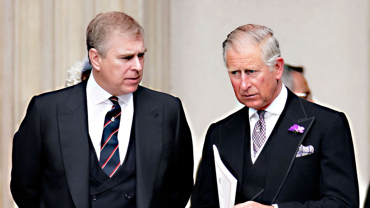 Prince Andrew talking to Prince Charles who listens with a serious expression on his face.