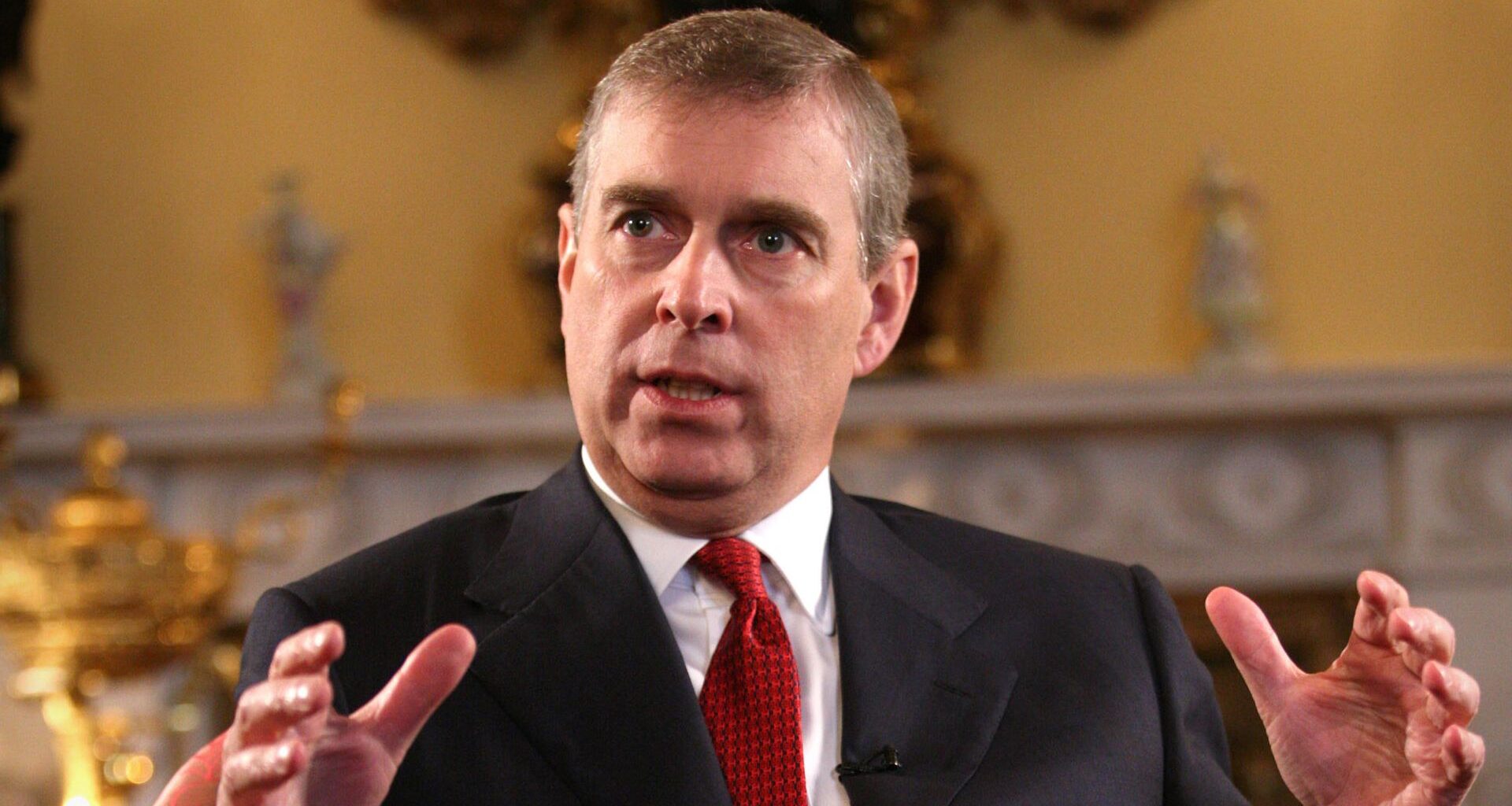 Ex-Prince Andrew wears a suit with a white shirt and a red tie and holds his hands in the air