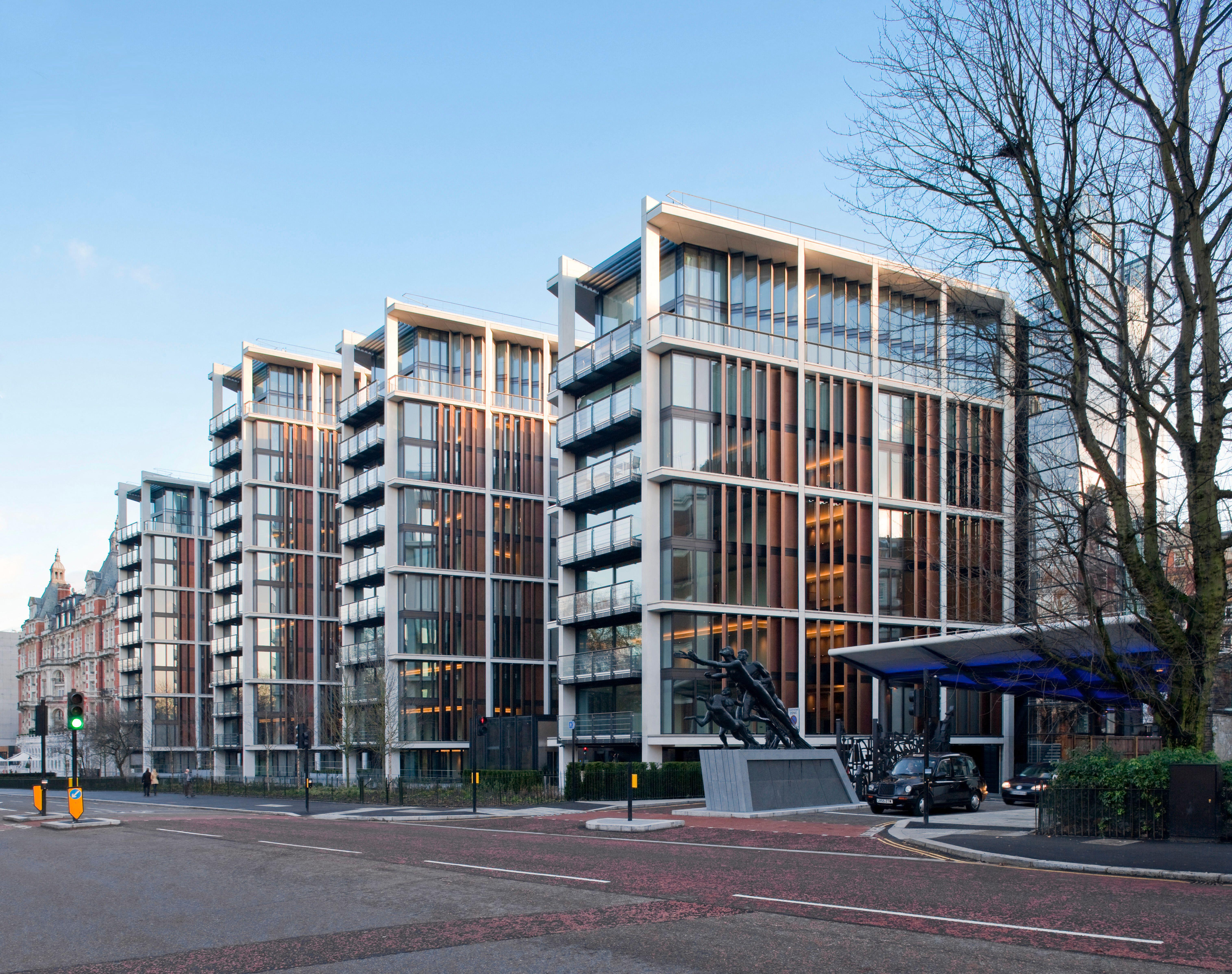 One Hyde Park building, with its many windows and balconies, and a bronze sculpture in front, stands across the street from a red brick building.