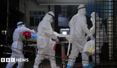 A picture of 3 people wearing white suits. They have masks on.