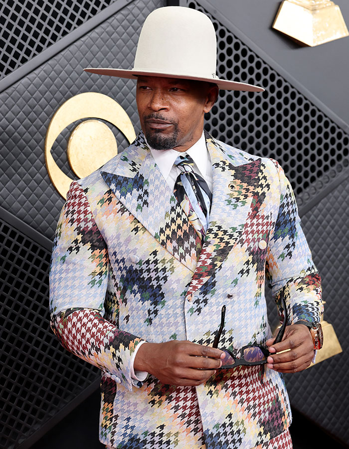 Jamie Foxx in a multicolored suit and wide-brimmed hat posing on the Grammy red carpet during a viral moment.
