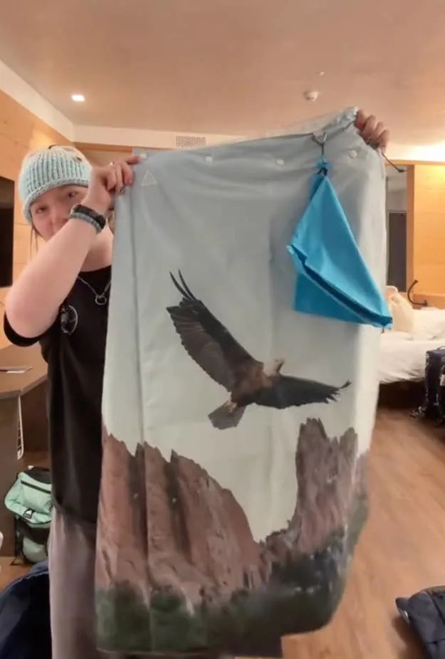 Person holding up a towel with an eagle printed above rock formations, indoors