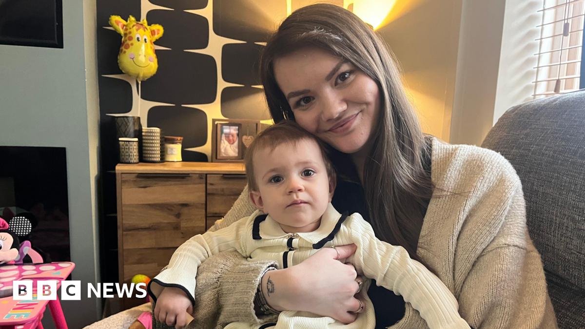Leah Cullen, who has long dark hair and dressed in a cream cardigan, sits with her daughter Aria on her lap in their home in Blyth.