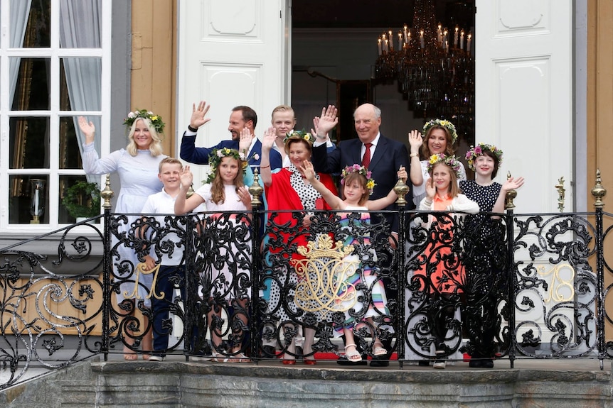 A group of people in formal attire standing on a balcony and waving