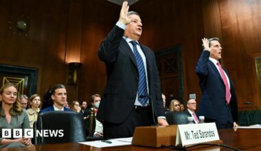 Two men wearing suits raise their right hands as they are sworn in for a Senate hearing in a courtroom