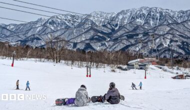 Snowboarders at the top of a ski slope with jagged mountain background