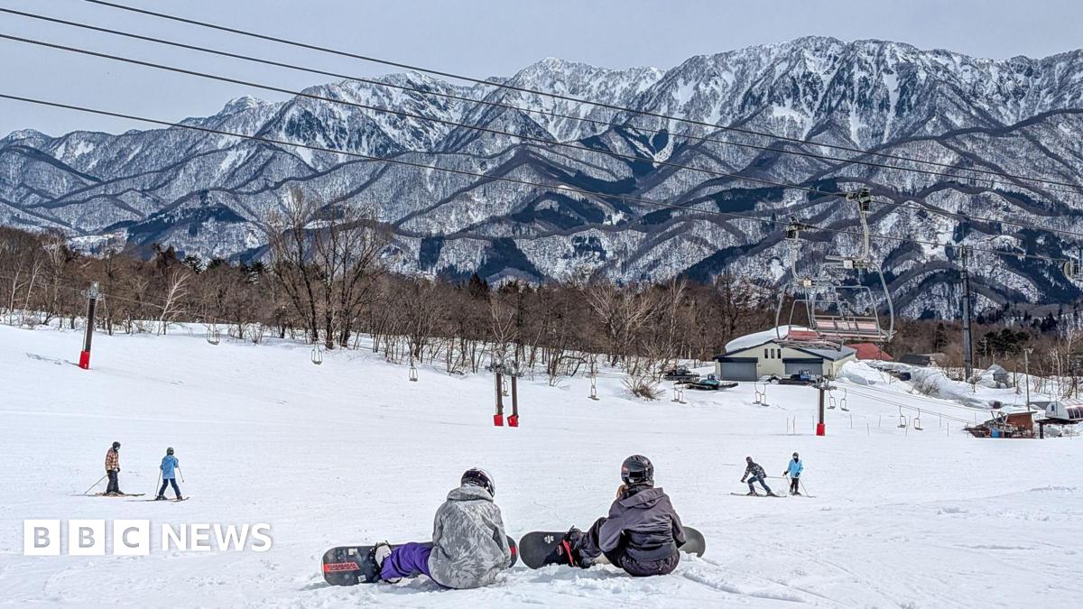 Snowboarders at the top of a ski slope with jagged mountain background
