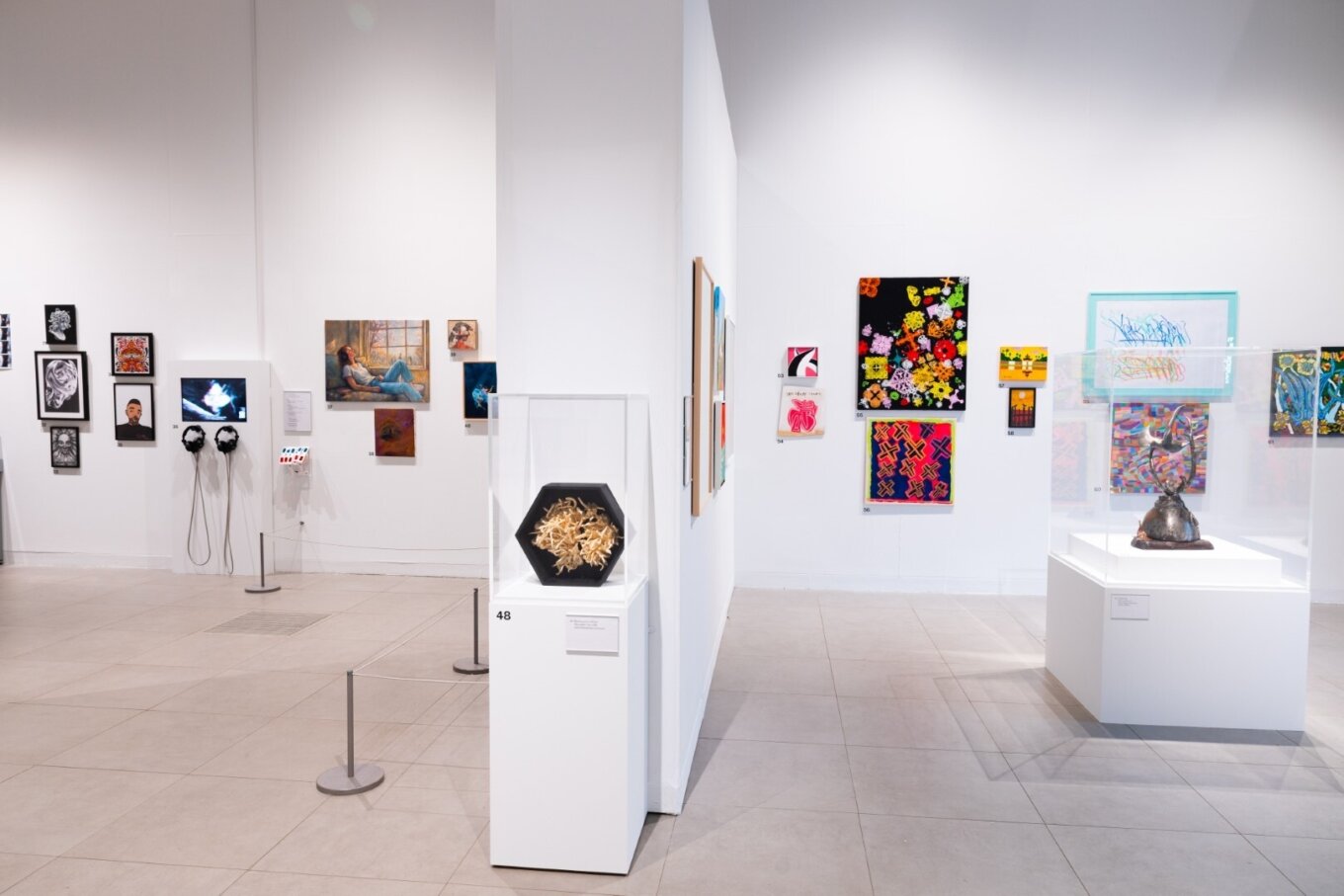 A photo of dozens of paintings and pieces of art hung up salon-style on the white walls of an art gallery