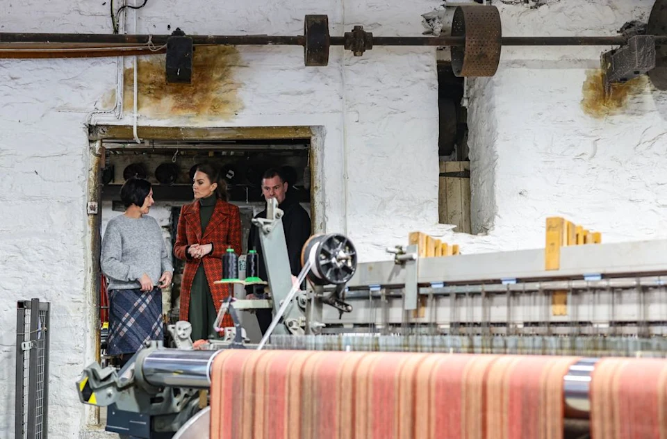 Princess Kate wearing an orange coat standing in the door of a woolen mill