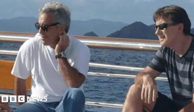 Undated image shows Jeffrey Epstein and Peter Mandelson onboard a yacht in an unspecified location. Epstein is wearing a white t-shirt, blue jeans and sunglasses. He has fairly short white hair and is wearing a watch. Mandelson is wearing a grey and black horizontal striped t-short, black shorts and sunglasses.