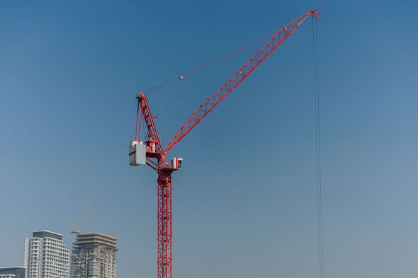 Red construction crane towering against a clear blue sky with modern buildings under construction visible in the background