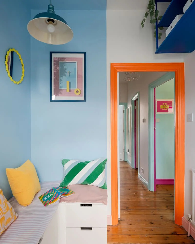 Colorful hallway with blue walls, orange door frame, and a cozy bench with decorative pillows and books.