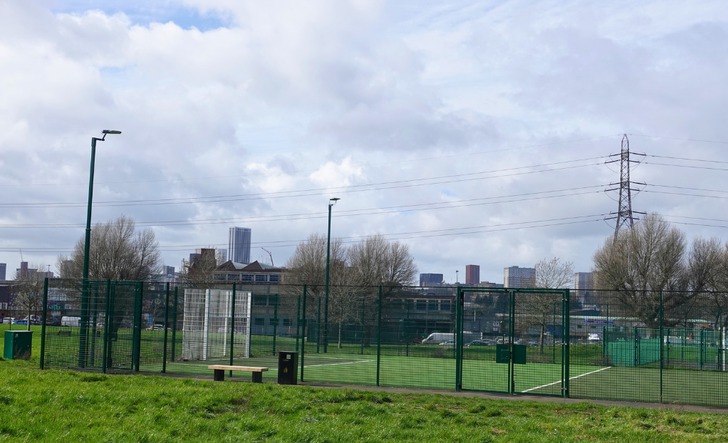 Adderley Park playzone - astro turf pitch with green fencing and lighting around it - birmingham skyline in the background