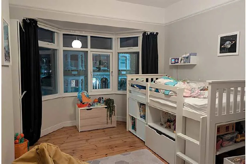 Cozy children's bedroom featuring a loft bed, wooden flooring, a storage chest, and colorful decor items.