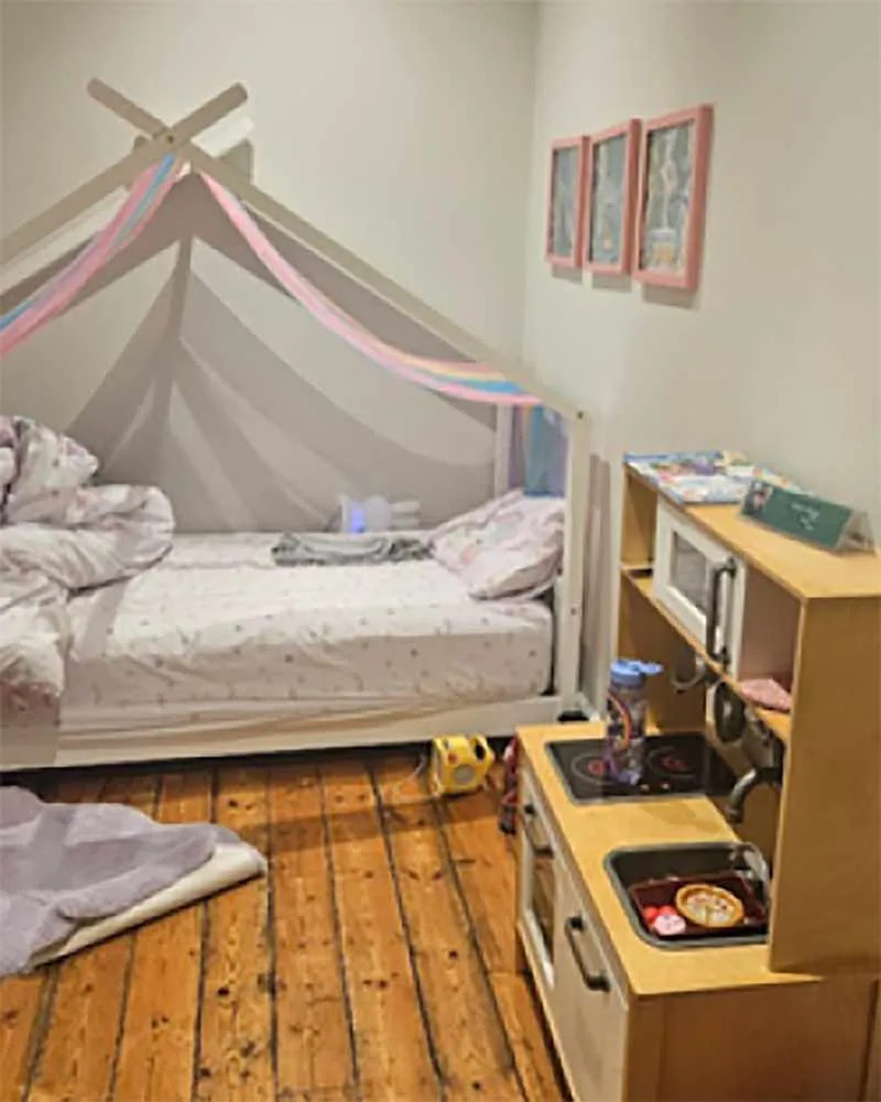 Cozy children's bedroom featuring a bed with a canopy, wooden floor, and a play kitchen with toy food.