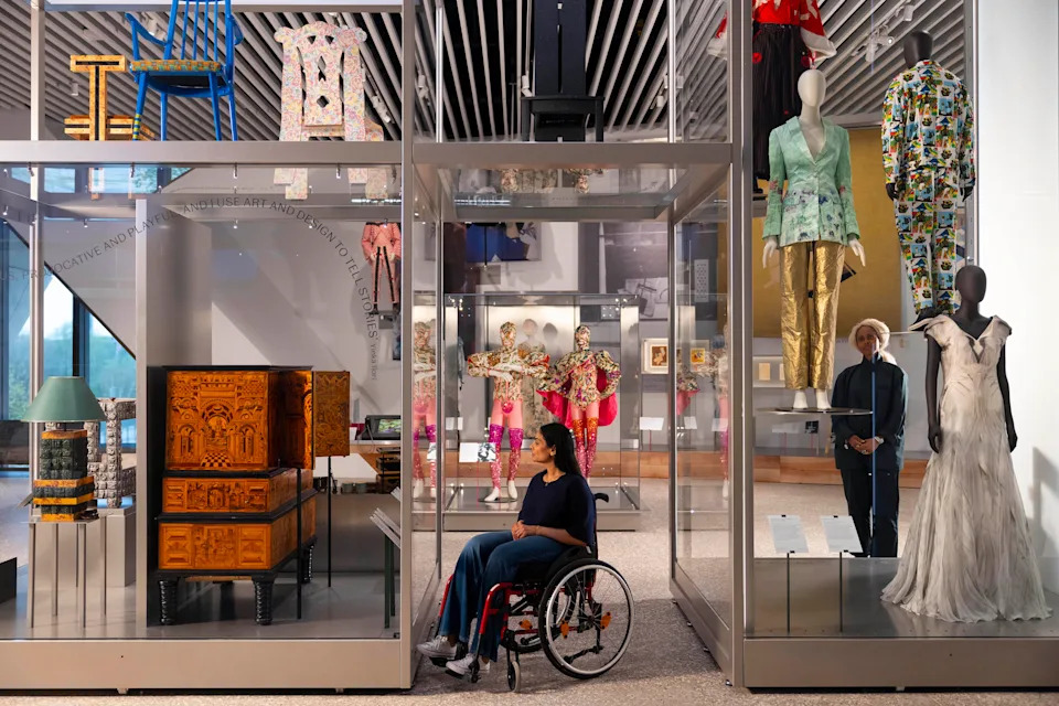 A woman in a wheelchair looking at historic and contemporary objects including Leigh Bowery ballet costumes and Alexander McQueen fashion, unveiled at V&A East Museum