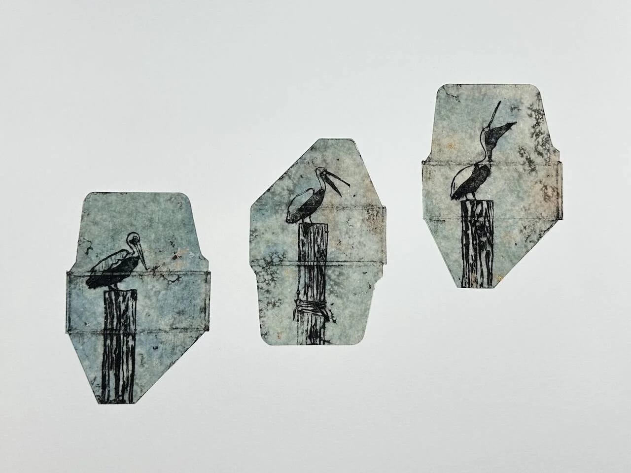 a collagraph print made in the outline of three small, flattened, cardboard cartons with imagery of pelicans sitting on wooden posts
