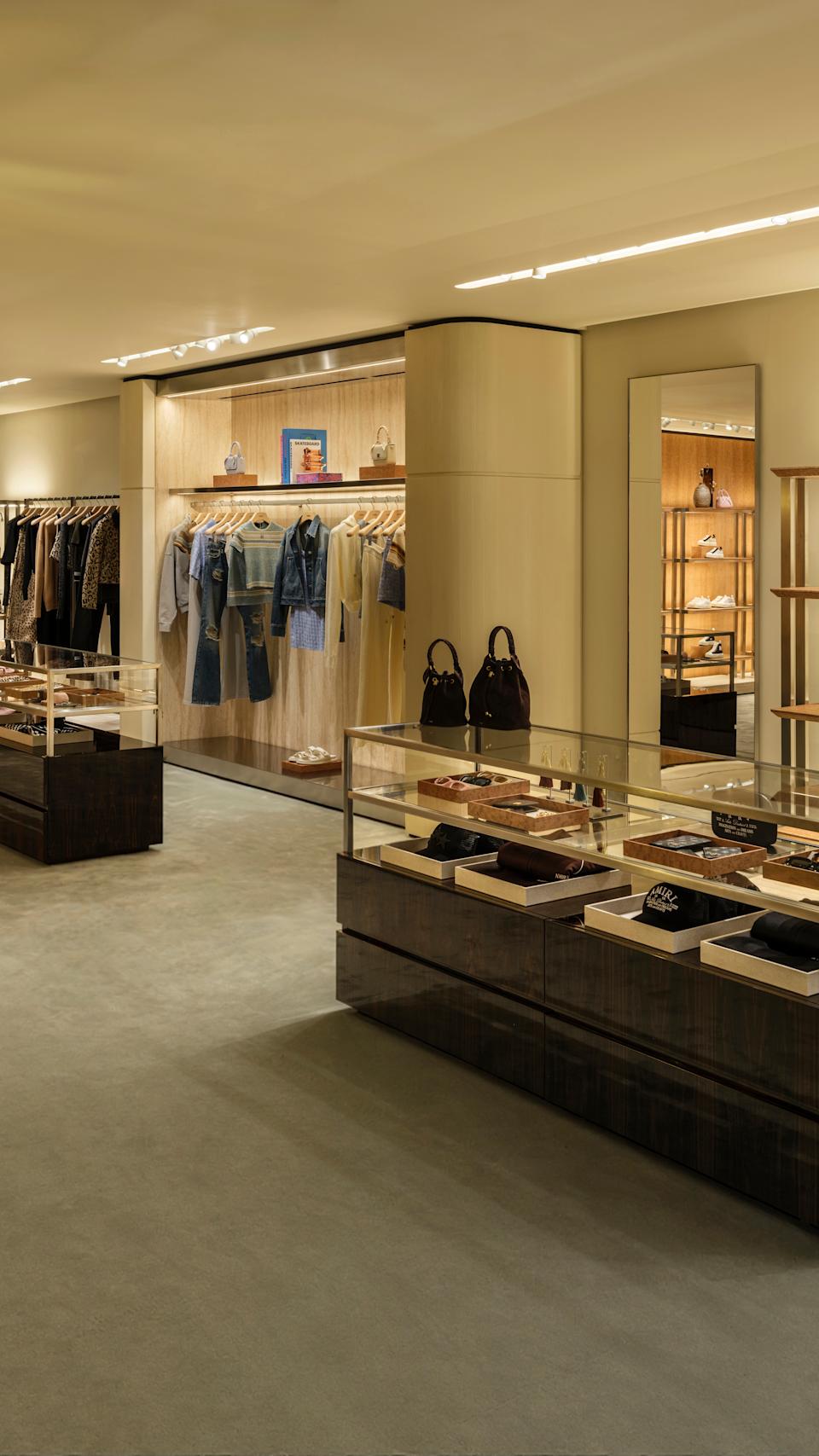 A luxurious clothing store interior with racks of clothes, display cases, and handbags on shelves under warm lighting.