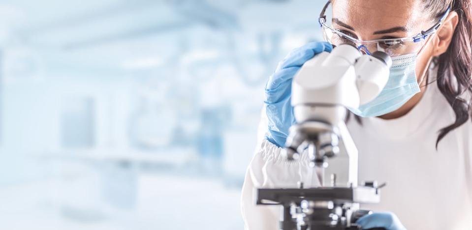 A person in a lab is gazing into a microscope.