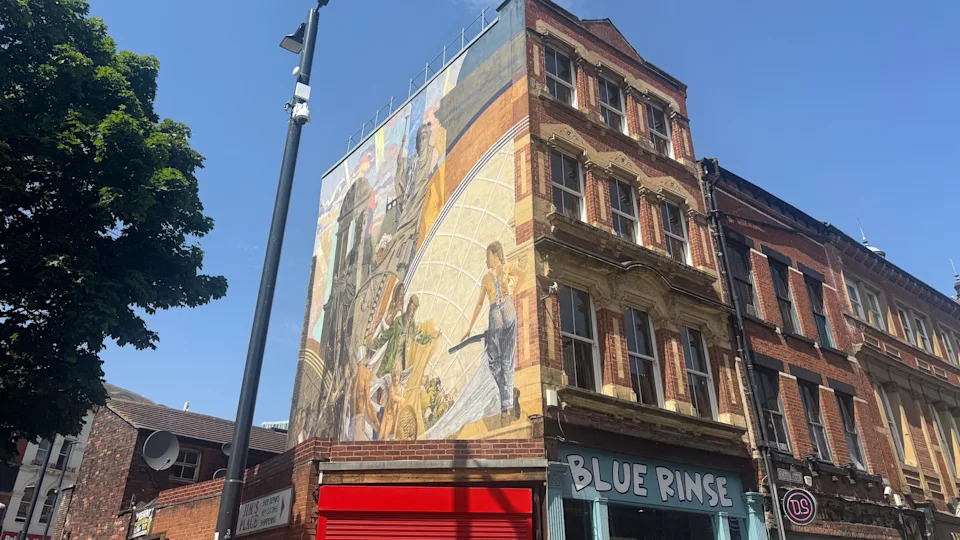 A building in Leeds which has a mural on the side which is called Cornucopia. The building is red brick and has shops on the ground floor, including one called Blue Rinse. 