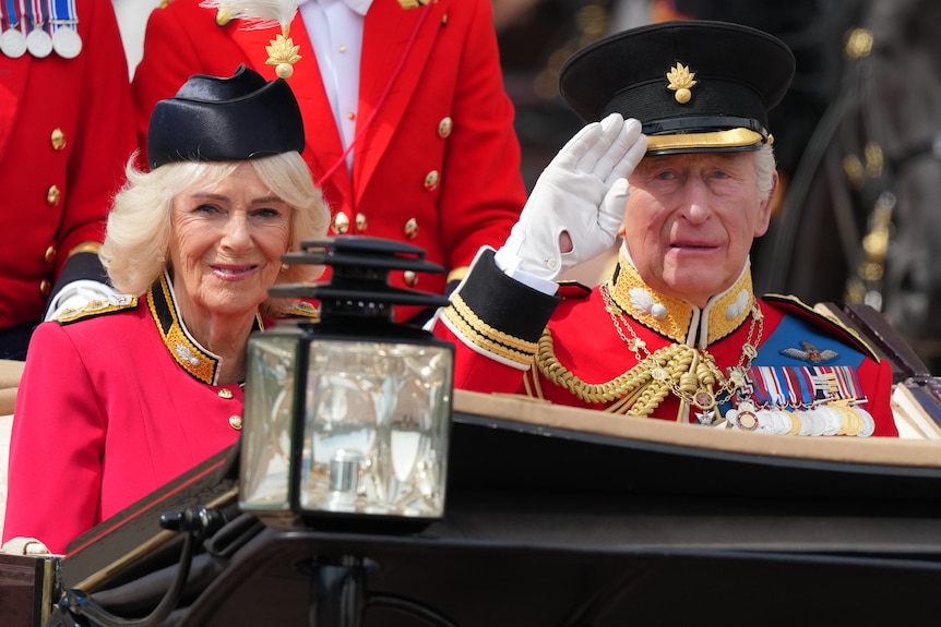 The king and queen in traditional dress sit in a carriage while the king waves.