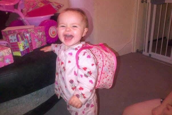 A young child wearing a backpack smiles at the camera.